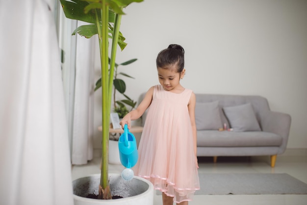 Active little preschool kid girl watering plants with water can at home