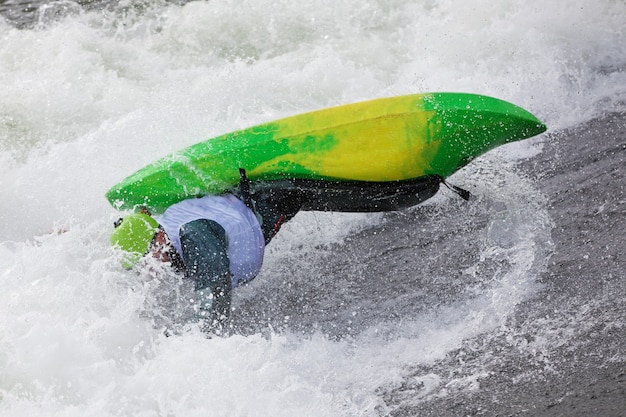 An active male kayaker rolling and surfing in rough water