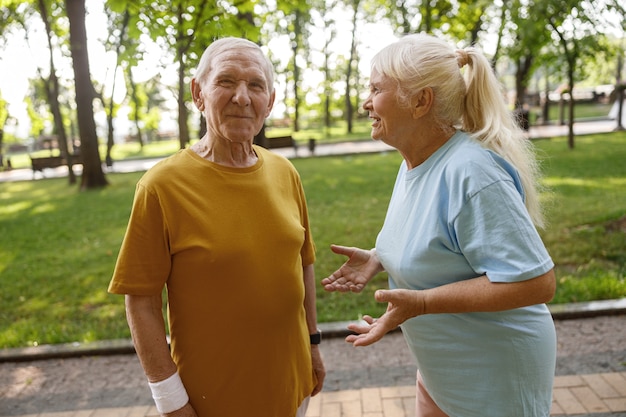 Активная зрелая женщина разговаривает с позитивным мужчиной на тренировке в зеленом городском парке