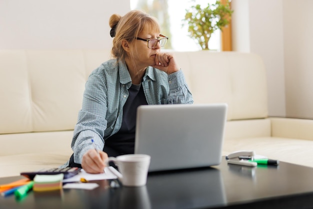 Active mature woman using a laptop for remote work from the\
home office video conference video meeting senior teacher leads\
webinar