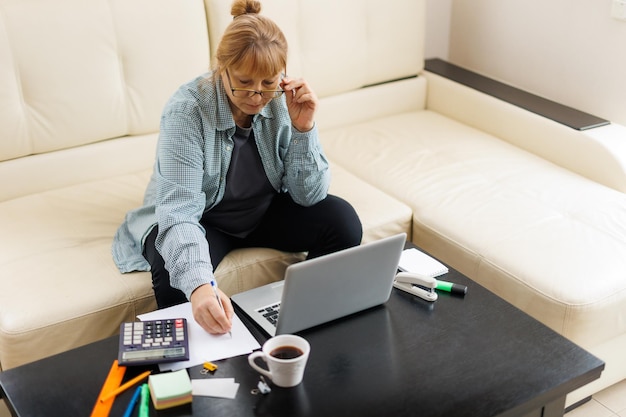 Active mature woman using a laptop for remote work from the home office Video conference video meeting Senior teacher leads webinar