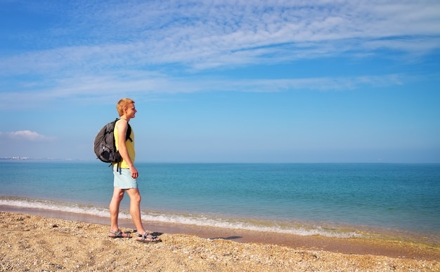 Active men with backpack on the shore. Man admiring nature by the sea