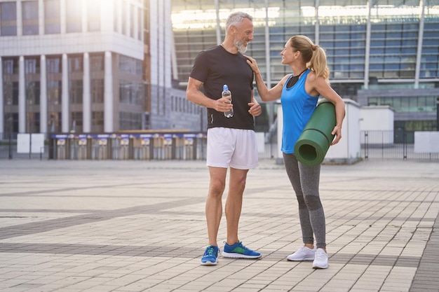 Active middle aged couple in sportswear doing sports together in the city standing outdoors with