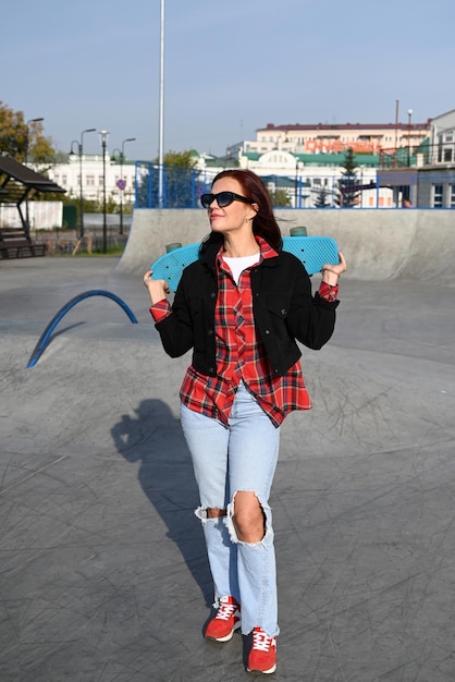 An active middleaged woman rides a skateboard on an empty road or highway An ordinary city woman relaxing on a skateboard after work The concept of a modern lifestyle