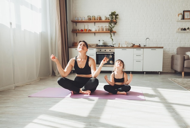 An active mother and a little daughter in black suits are\
engaged in fitness yoga physical exercises at home sports\
family