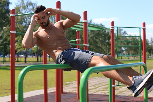 Active muscular athlete doing abs training and crunches outdoor, working out.