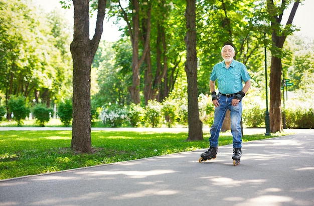 Vecchiaia attiva. felice uomo anziano pattinaggio a rotelle all'aperto. uomo anziano che si diverte a fare sport nel parco estivo soleggiato. concetto di stile di vita sano, copia spazio