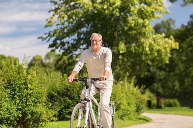 Active old age, people and lifestyle concept - happy senior man riding fixie bicycle at summer park