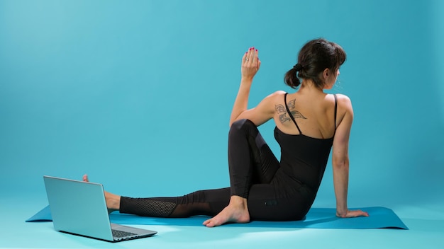 Активный человек растягивает мышцы тела после фитнес-тренировки, смотрит онлайн-видео по пилатесу на ноутбуке. Женщина использует оздоровительный урок, чтобы растянуть руки и ноги, восстанавливаясь после тренировки.