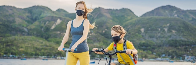 Active school kid boy and his mom in medical mask riding a bike with backpack on sunny day happy