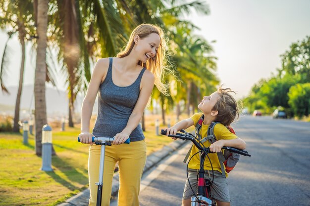 Active school kid boy and his mom riding a bike with backpack on sunny day Happy child biking on way to school Safe way for kids outdoors to school