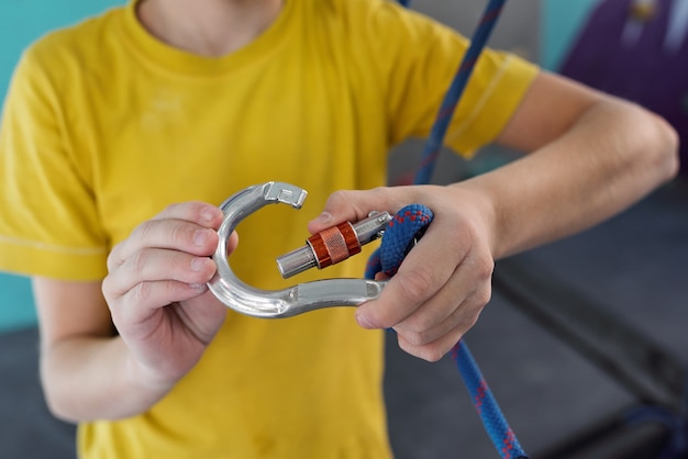 Active schoolboy locking carabiner with thick blue rope while getting ready for climbing practice at leisure