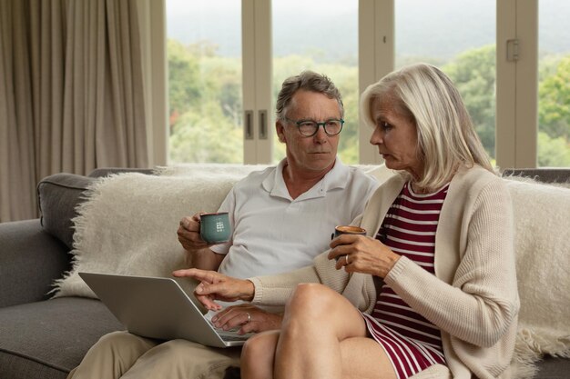 Photo active senior couple discussing over laptop while having coffee on sofa in a comfortable home