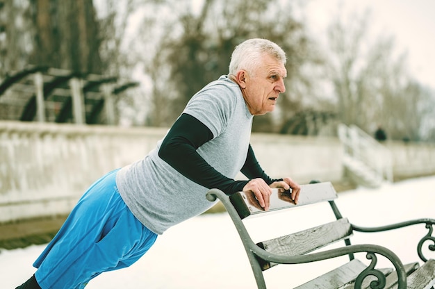 Photo active senior man athlete doing push ups on the bench and doing exercises by the river during the winter training outside in. copy space.