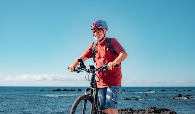 晴れた日をビーチで電動自転車で楽しむアクティブシニア男性 本格的なリタイア生活と健康的なライフスタイルのコンセプト 海の向こうのホライゾン