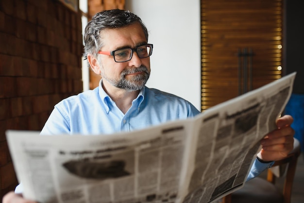 Active senior man reading newspaper and drinking coffee in restaurant