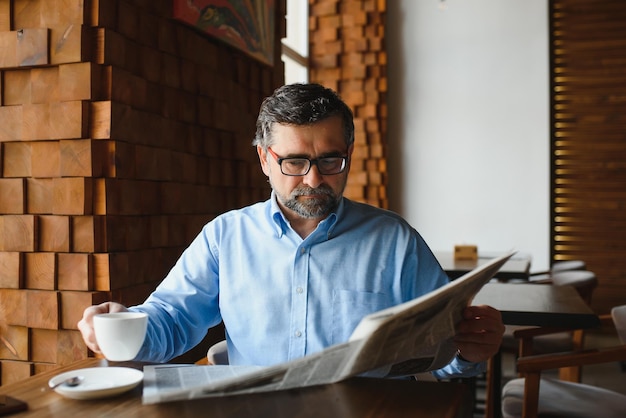 Active senior man reading newspaper and drinking coffee in restaurant