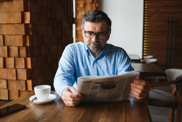 Active senior man reading newspaper and drinking coffee in restaurant