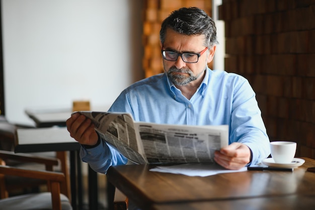 Active senior man reading newspaper and drinking coffee in restaurant