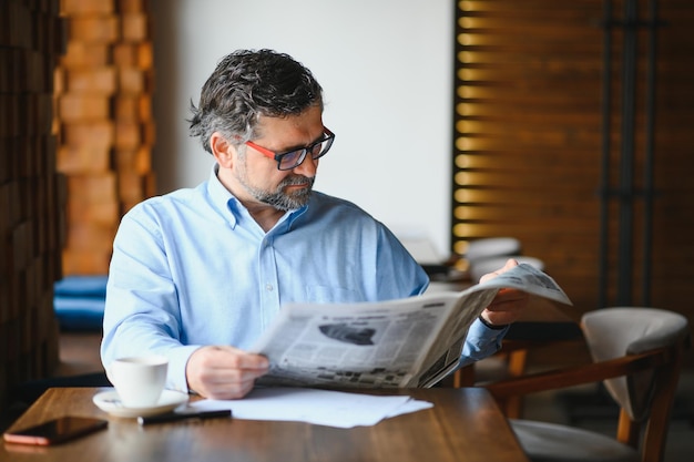 Active senior man reading newspaper and drinking coffee in restaurant