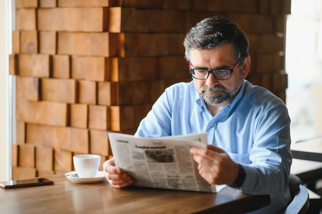 Foto uomo anziano attivo che legge il giornale e beve caffè nel ristorante