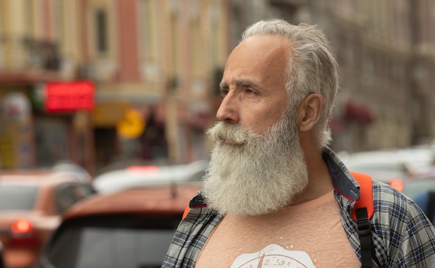 Active senior man walking in the city. Portrait of senior man with a beard while standing outside.