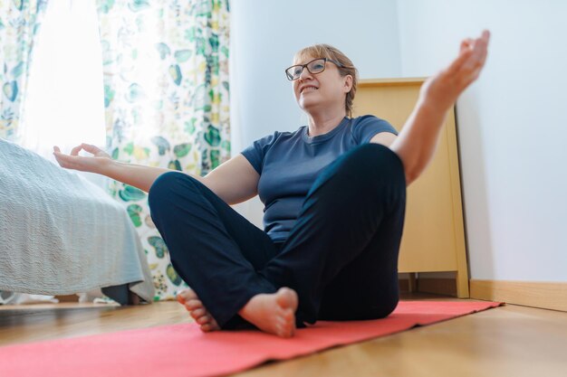 Active senior woman doing abs exercises on yoga mat at home and smiling at camera