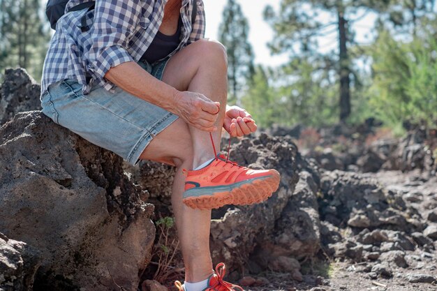 Photo active senior woman on a mountain hike sits down to better tie her hiking boots mature woman appreciating a healthy lifestyle in the outdoors