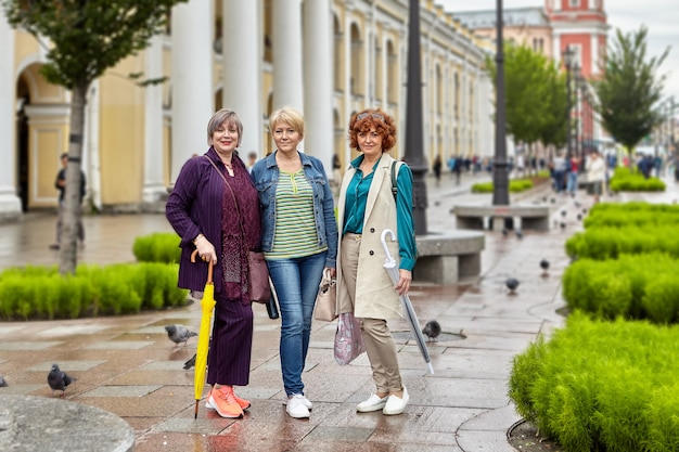 Active senior women stand on the street of European city in rainy weather and look into the camera lens.