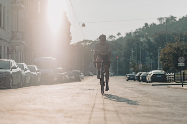 Active sportsman in safety helmet and mirrored glasses practicing in cycling on street of big city Morning sunlight on background Outdoors workout