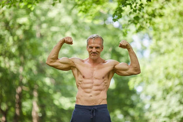 Photo active sporty aged man standing shirtless somewhere in city park demonstrating his well-muscled body on camera