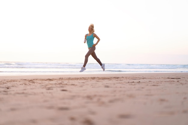 활동적인 스포티 한 여성은 건강과 건강을 유지하기 위해 물 수영장에서 바다 서핑을 따라 달리고 태양이있는 일몰 모래 해변 배경 여성 피트니스 조깅 운동 및 스포츠 활동