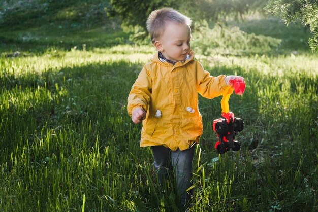 Активный малыш с игрушечной машинкой гуляет на улице весной