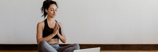 Donna attiva che impara lo yoga online tramite un laptop