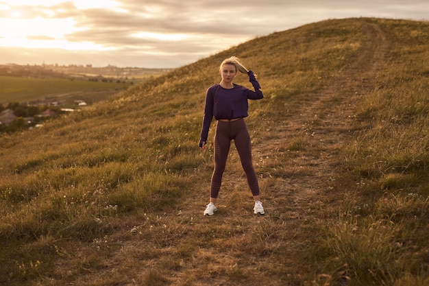 Active woman in sportswear standing on hill