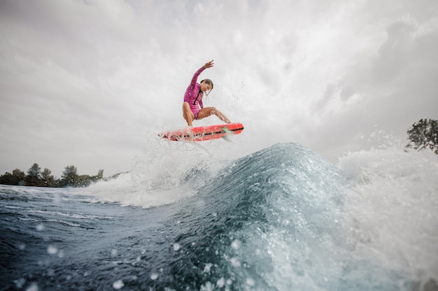 Active woman surfer jumping up the blue splashing wave against sky