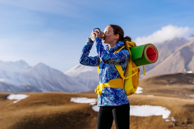 Фото Активная молодая девушка в синей куртке пьет горячий чай, путешествует по кавказскому хребту