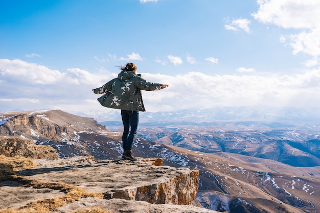 Active young girl travels, stands on the edge of the mountain and enjoys nature