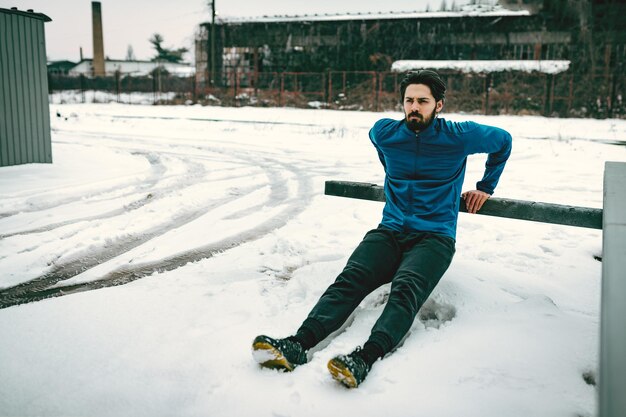 Active young  man stretching and doing exercises in the public place among old railroad during the winter training outside in. Copy space.