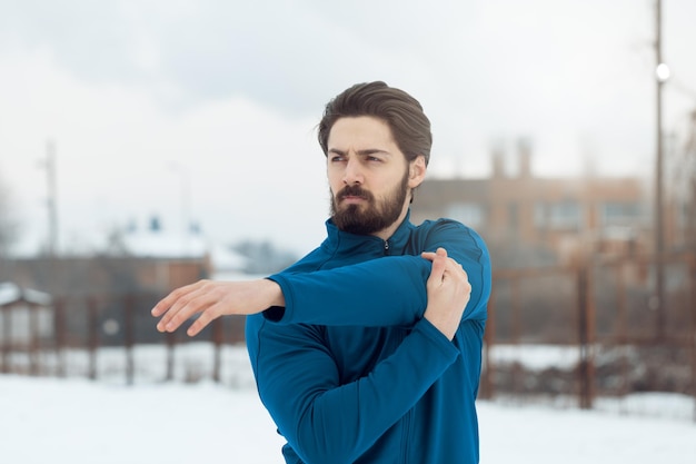 Active young man stretching and doing exercises in the public place during the winter training outside in. Copy space. Close up.