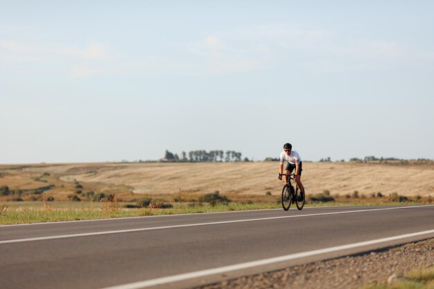 Photo active young man with athletic body cycling on road during sunny day