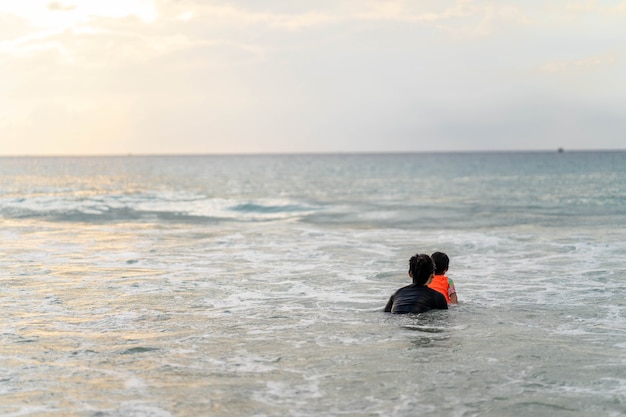 Active young mother and daughter in swimming suit playing at the beach against sunset at sea.