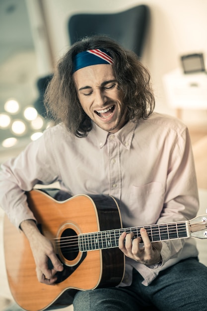 Active young performer. Long-haired handsome artist loudly singing and playing on guitar during personal repetition