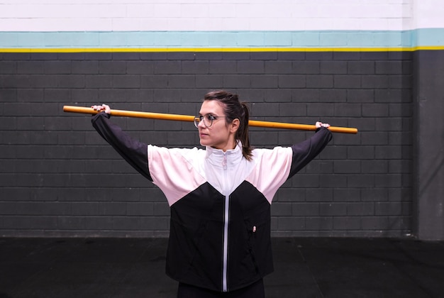 Foto giovane donna attiva che si allunga in palestra usando una bacchetta da yoga