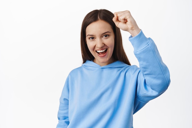 Activism. Young cheerful brunette woman fist pump, fighting for human rights, smiling and looking determined, chanting on pride parade, standing in hoodie against white background.