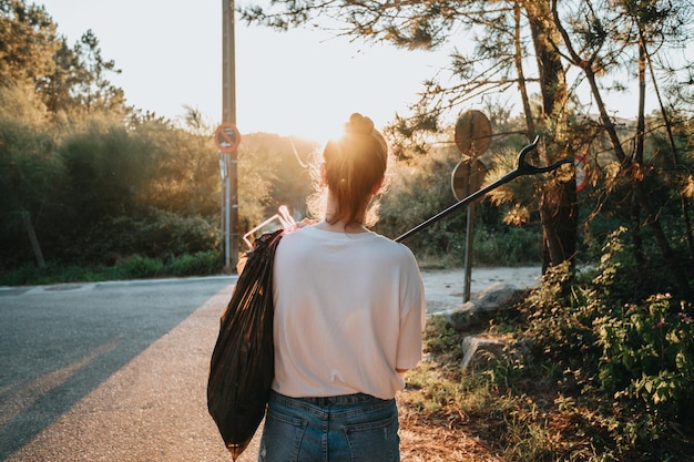 写真 カメラに向かって後ろ向きにゴミトングでゴミを拾う活動家の若い女性森の背景