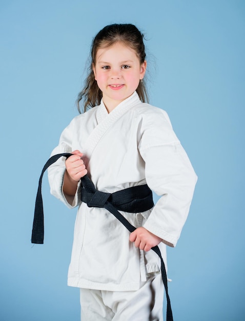 Activiteit en sport Sterk en zelfverzekerd kind Meisje klein kind in witte kimono met riem Karatevechter klaar om te vechten Karate sportconcept Zelfverdedigingsvaardigheden Karate geeft een gevoel van vertrouwen