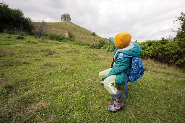 Activiteit op zonnige herfstdag jongen die de natuur verkent Kid draagt gele hoed en rugzak zit tegen de grote steen van Pidkamin, Oekraïne