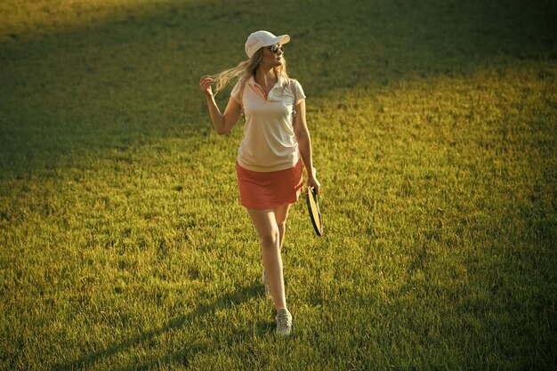 Активность, энергия, здоровье. Женщина-игрок с теннисной ракеткой гуляет по лужайке