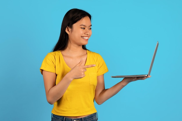 Ad and offer huge sale Happy young asian lady student in yellow tshirt point finger at computer screen